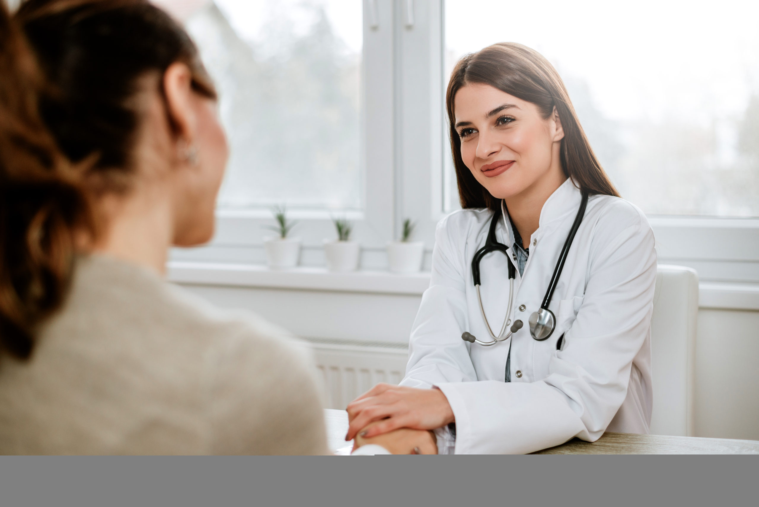 Friendly female doctor holding female patient's hand for encouragement and empathy.